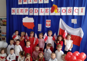Pamiątkowe zdjęcie dzieci na tle dekoracji z flagami i balonami.